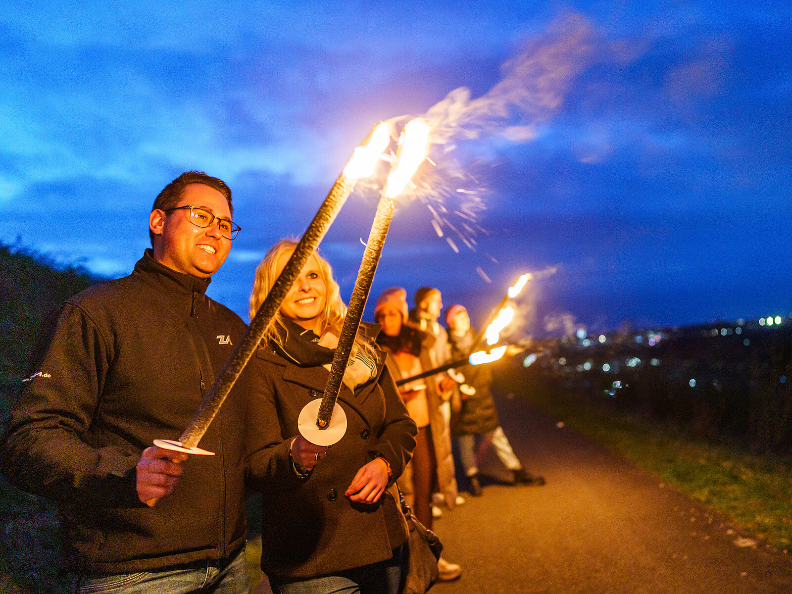 Fackelwanderung_Halde Hoheward_C_RVR_VWiciok Zwei Personen halten im Dunkeln ihre Fackeln aneinander, um die zweite Fackel zu entzünden.