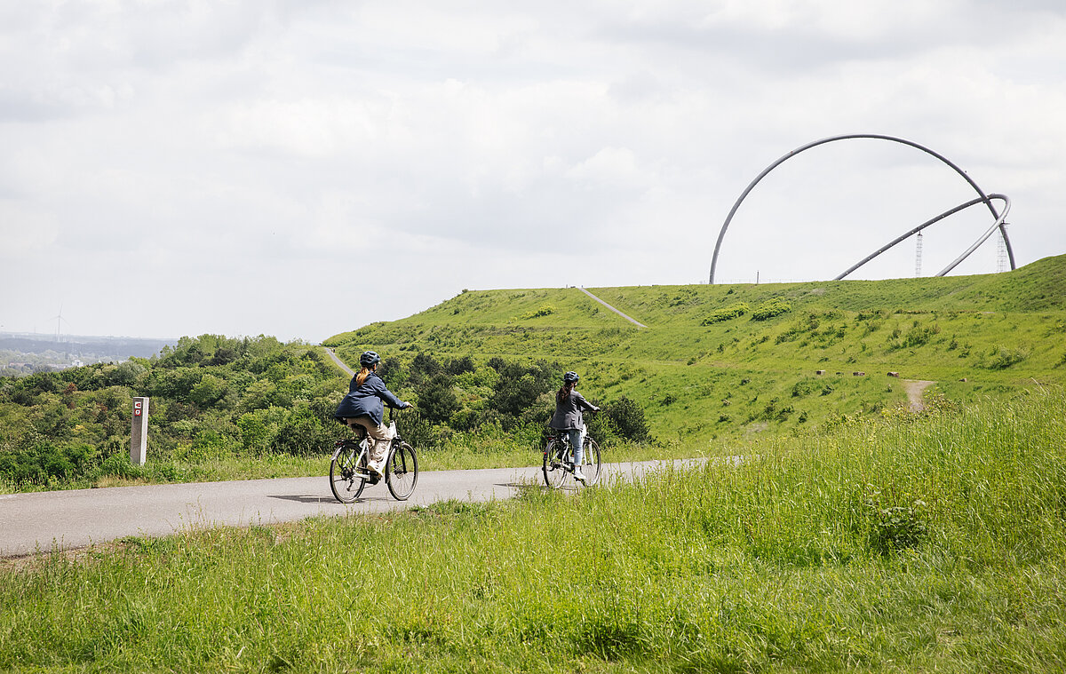 Zwei Fahrradfahrer fahren auf Pedelecs auf einer Straße auf der Halde Hoheward. Im Hintergrund ist das Horizontobservatorium zu sehen.