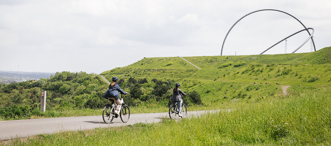 Zwei Fahrradfahrer fahren auf Pedelecs auf einer Straße auf der Halde Hoheward. Im Hintergrund ist das Horizontobservatorium zu sehen.