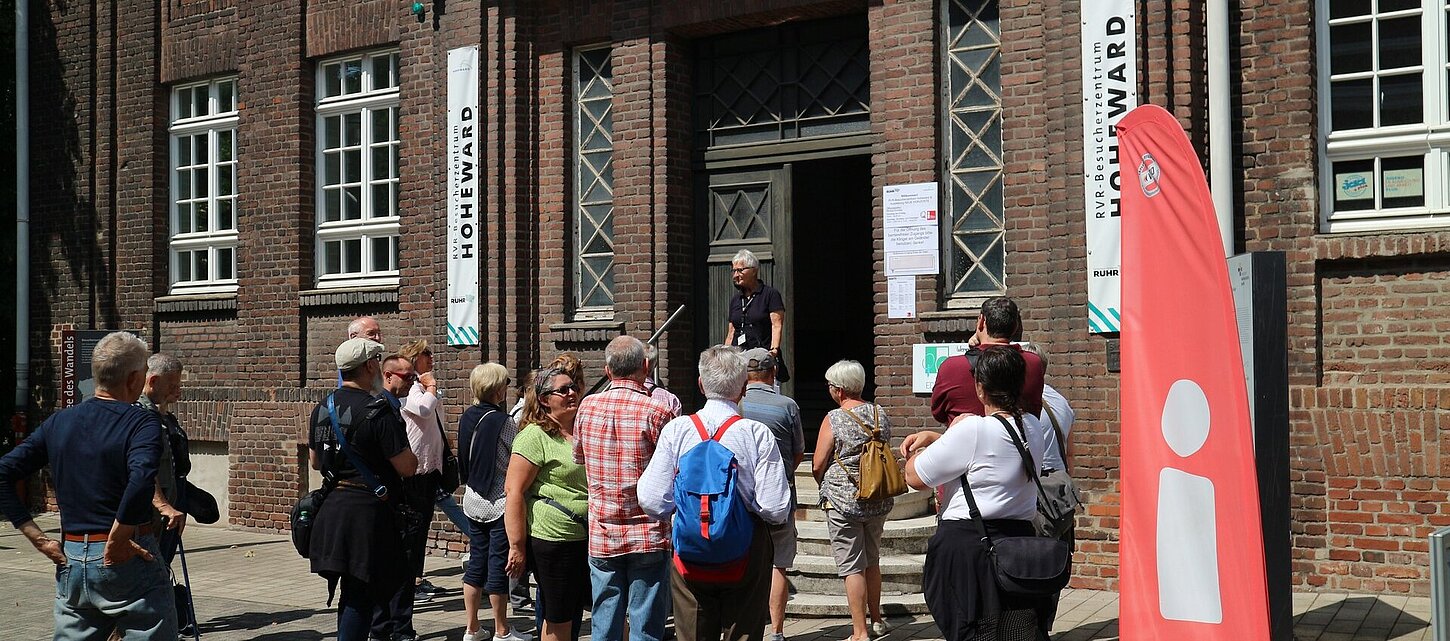 Eine Besuchergruppe mit Gästeführerin vor dem Eingang des Besucherzentrums
