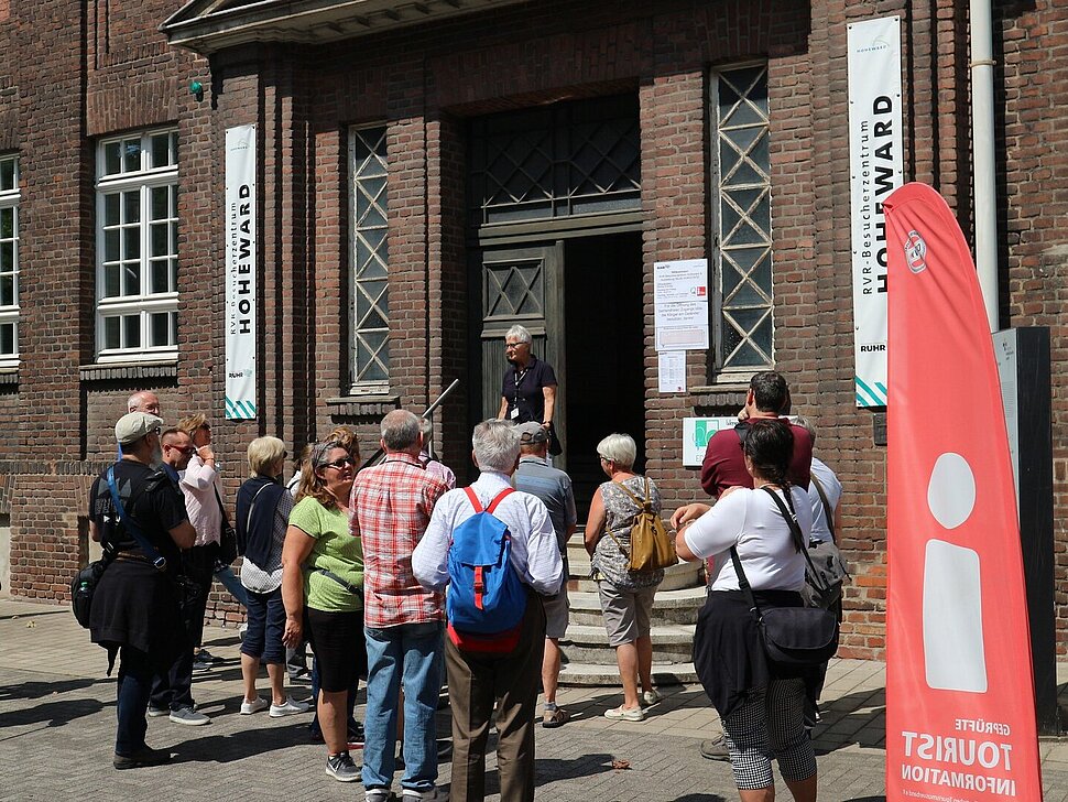 Eine Besuchergruppe mit Gästeführerin vor dem Eingang des Besucherzentrums