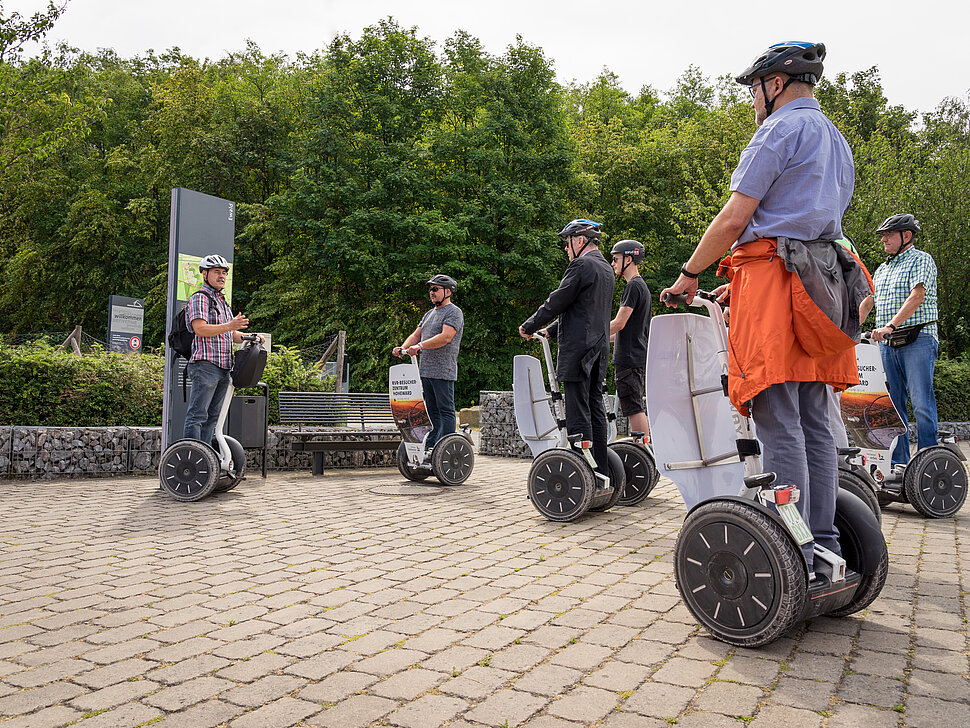 Eine Gruppe von Personen auf Segways, die vor einem Infoschild auf der Halde Hoheward angehalten haben um den Ausführungen ihres Gästeführers zuzuhören.