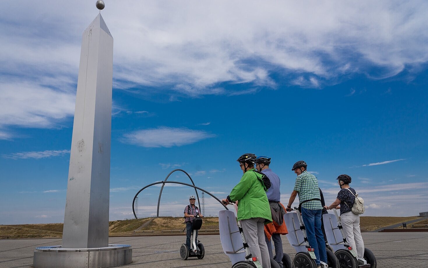 Eine Gruppe von Personen auf Segways steht neben dem Obelisken der Sonnenuhr auf der Halde Hoheward. Im Hintergrund sind die Stahlbögen des Horizontobservatorium zu sehen.