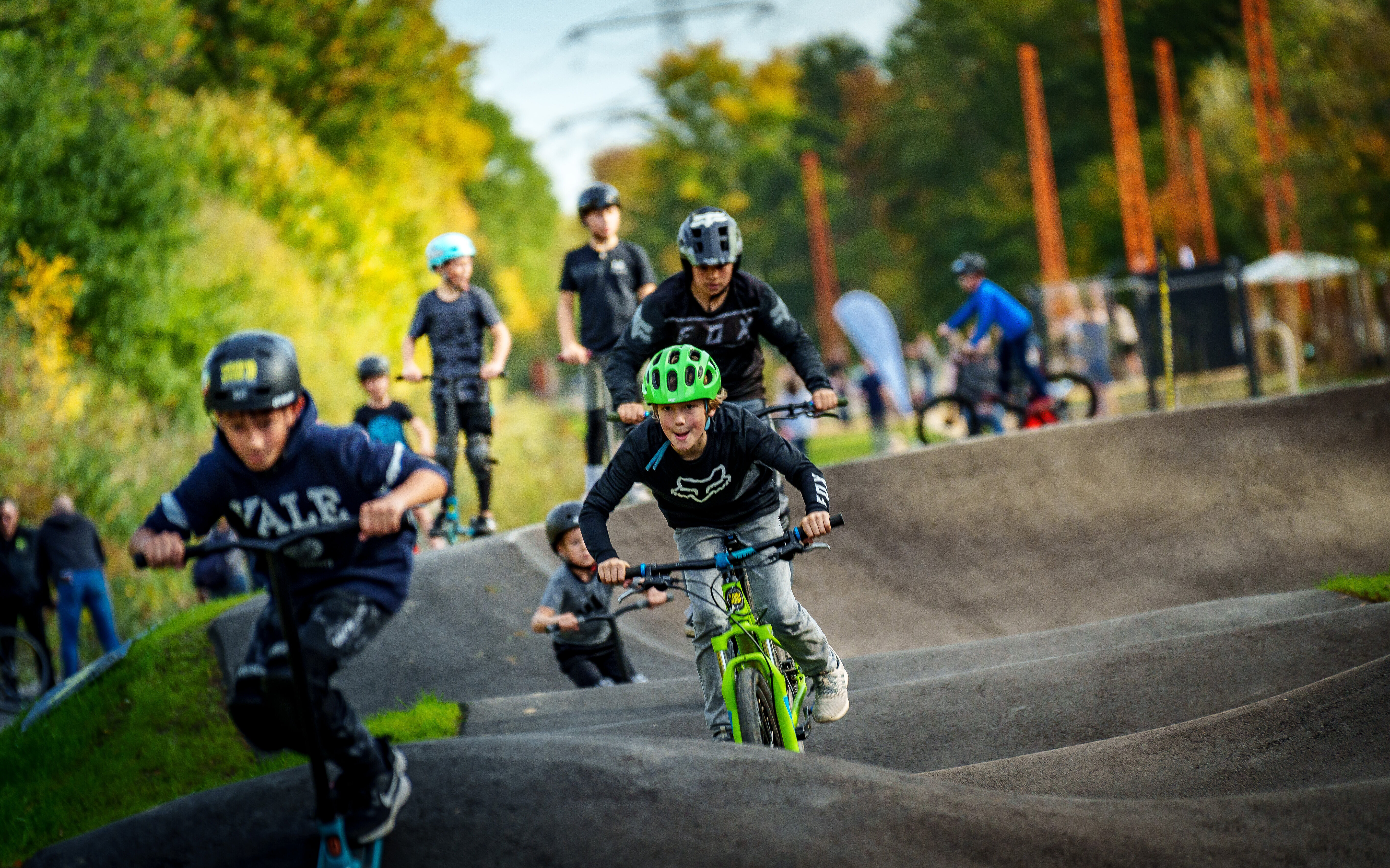 Mehrere Kinder auf verschiedenen Fahrgeräten (Fahrräder, Roller) nutzen den Pumptrack im AktivLinearPark an der Halde Hoheward.