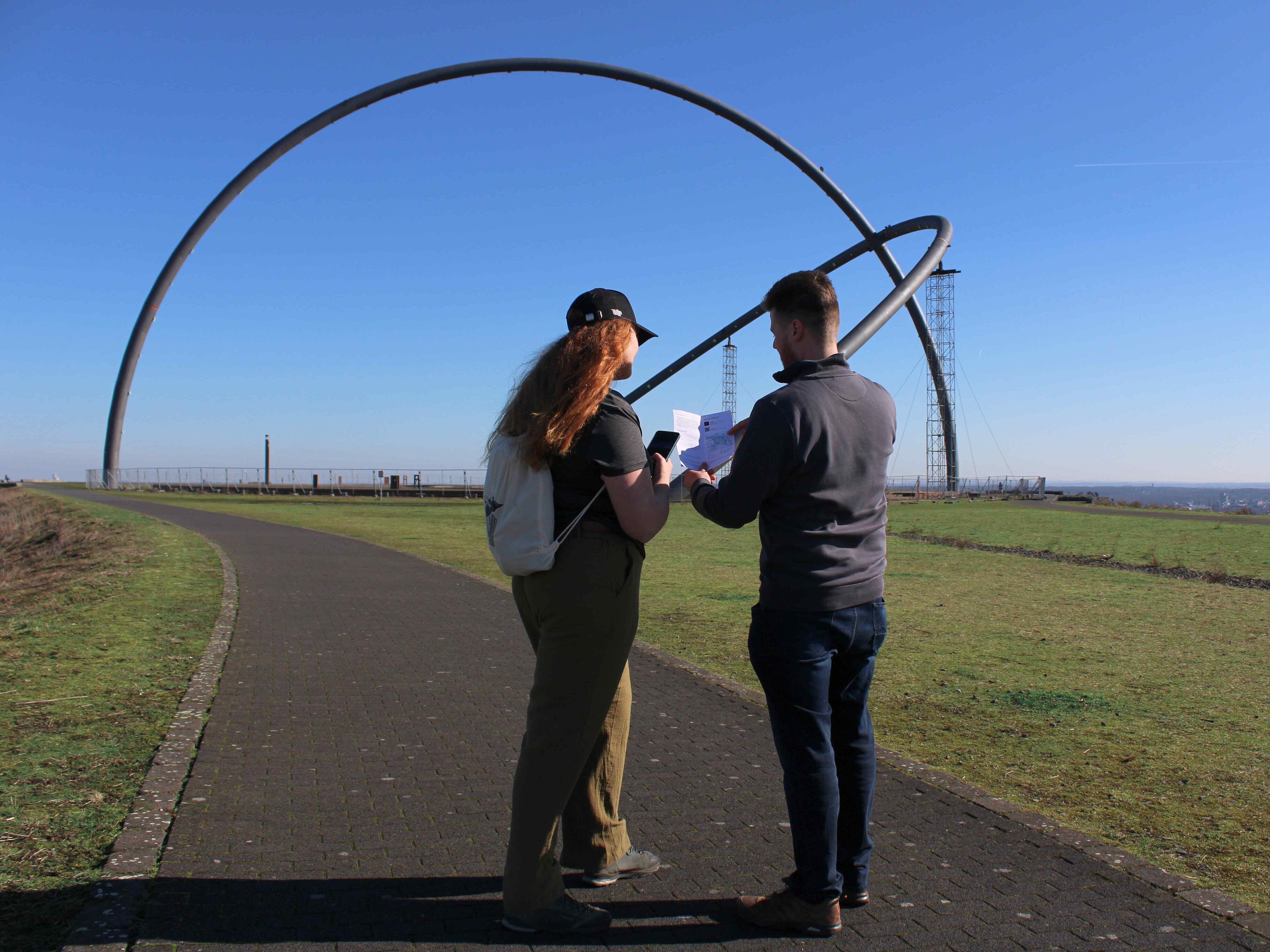 Zwei Personen stehen vor dem Horizontobservatorium und schauen auf ihr Handy und einen Flyer