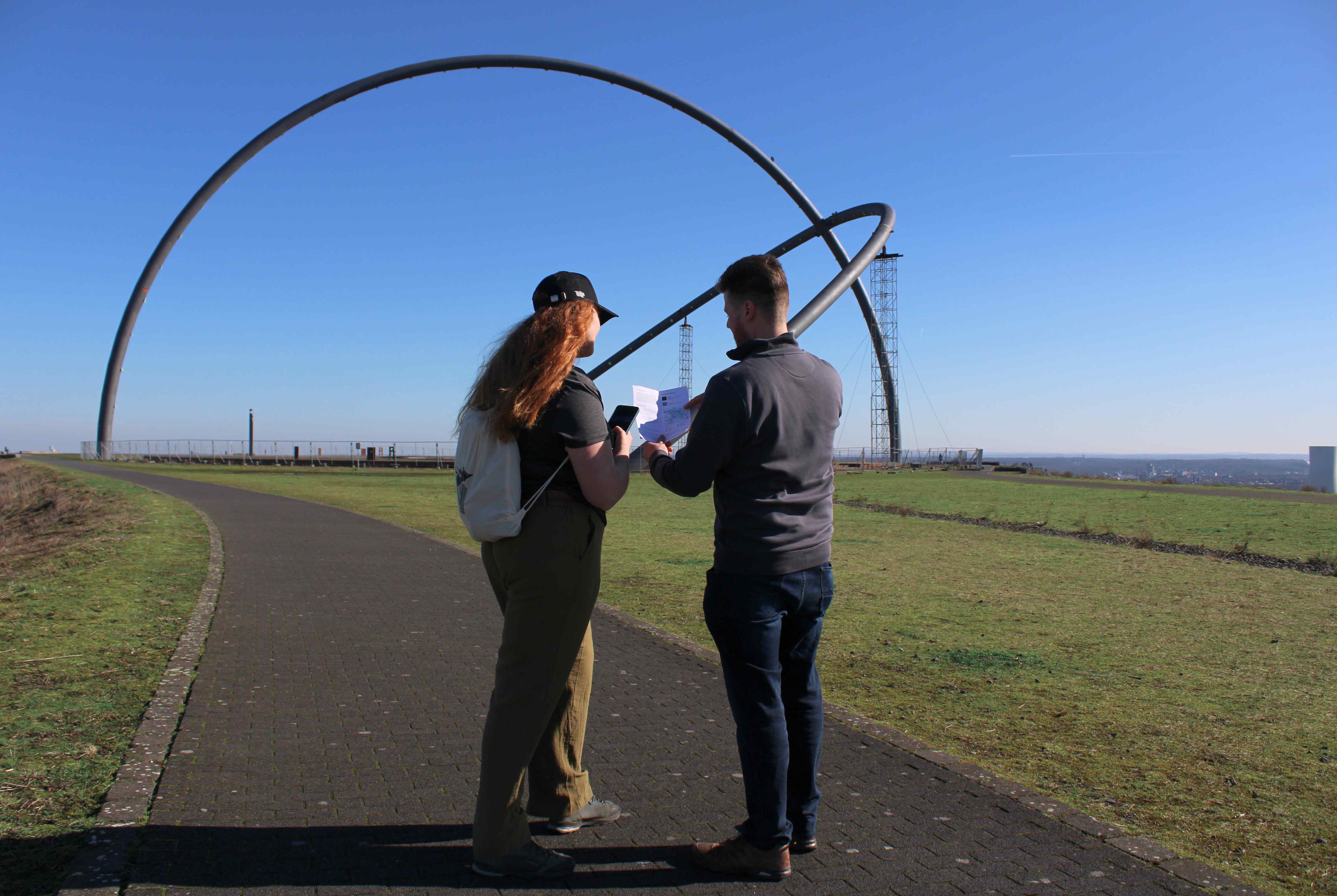 Zwei Personen stehen vor dem Horizontobservatorium und schauen auf ihr Handy und einen Flyer